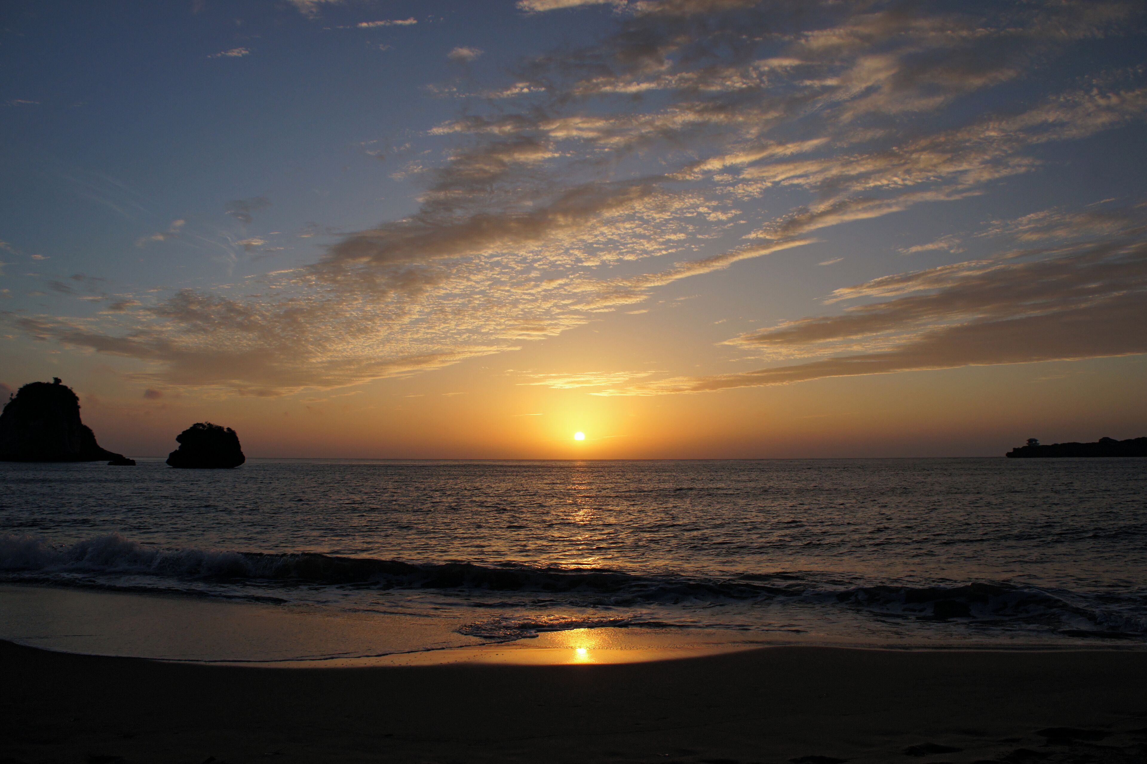 A sunset over the ocean with a beach and rock formations.