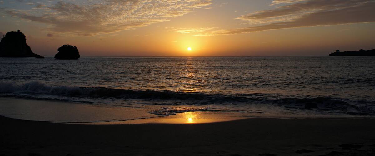 A sunset over the ocean with a beach and rock formations.