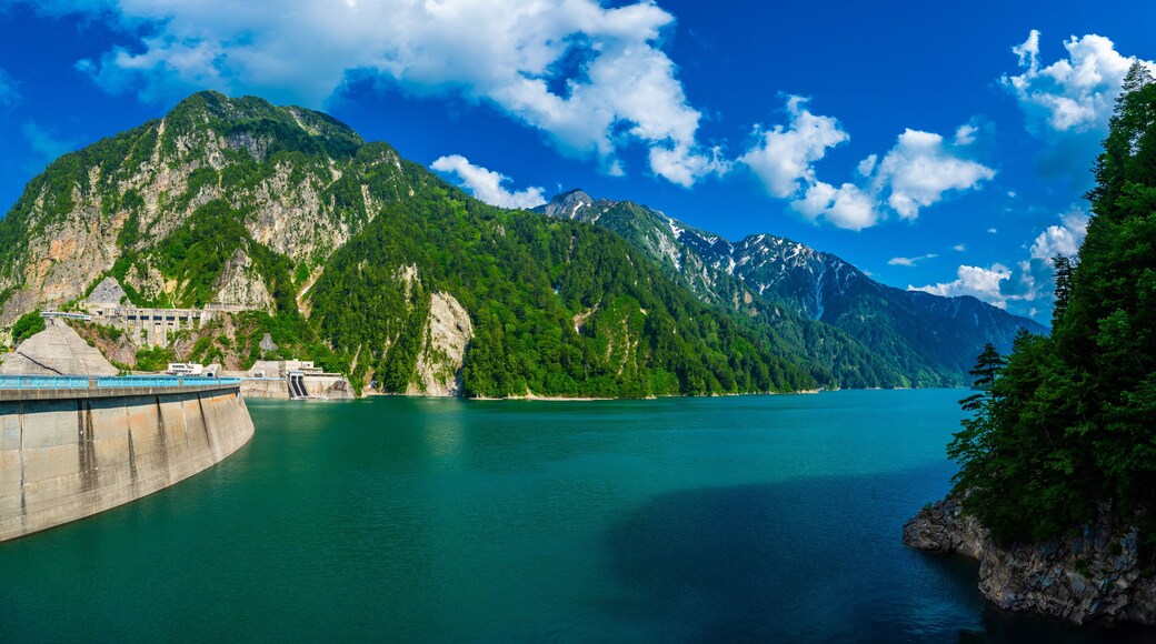 Panorama Beautiful scenery of Kurobe Dam on a brisk, with colorful lakeside mountains and crystal clear lake water under blue sunny sky in Tateyama Kurobe Alpine Route, Toyama, Japan