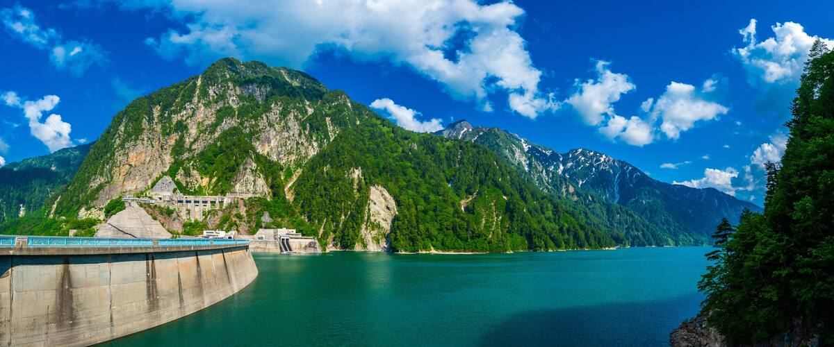 Panorama Beautiful scenery of Kurobe Dam on a brisk, with colorful lakeside mountains and crystal clear lake water under blue sunny sky in Tateyama Kurobe Alpine Route, Toyama, Japan