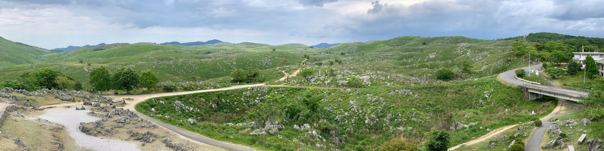 A winding road through a hilly landscape with a bridge and a building on the right.