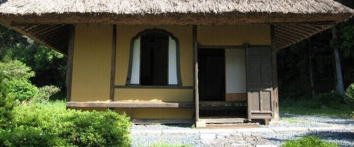 A thatched-roof hut with a yellow facade, surrounded by greenery.