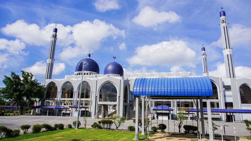 A mosque with two large domes, a minaret, and a covered entrance.