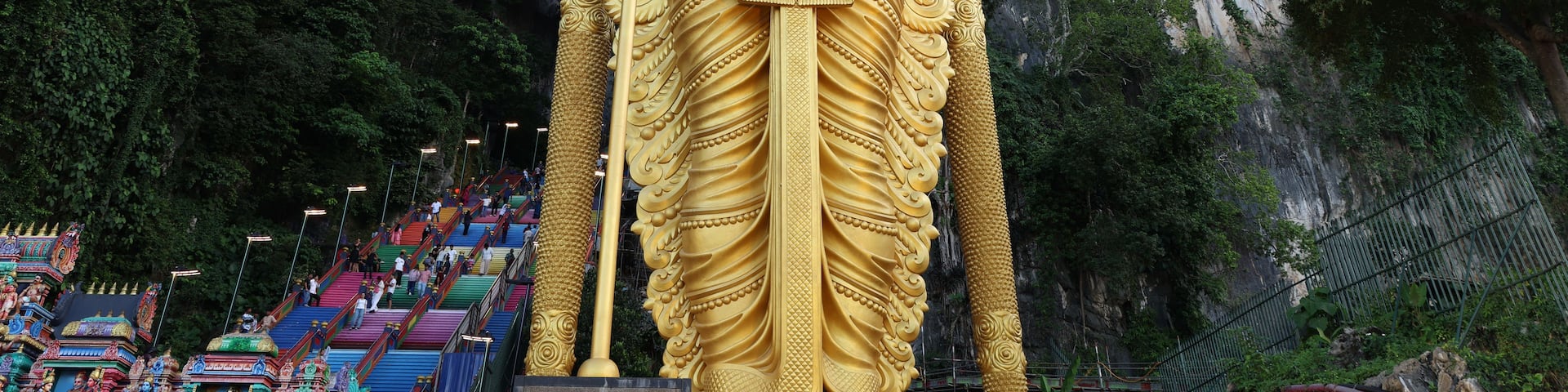A large golden statue of a deity holding a staff, set against a backdrop of lush green cliffs.