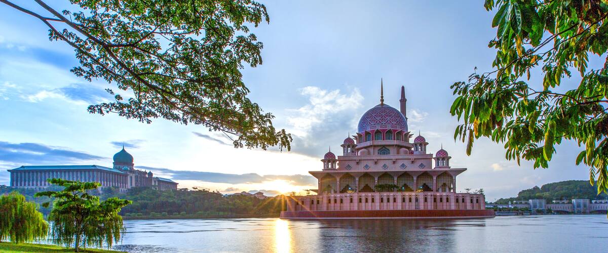 A large, ornate building with a dome and multiple minarets, situated by a calm body of water.