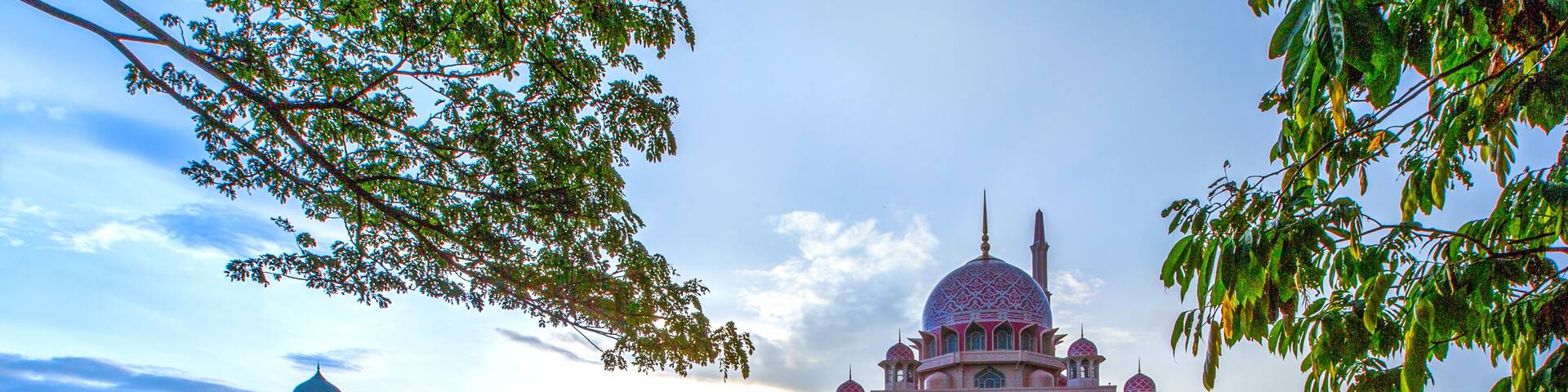 A large, ornate building with a dome and multiple minarets, situated by a calm body of water.