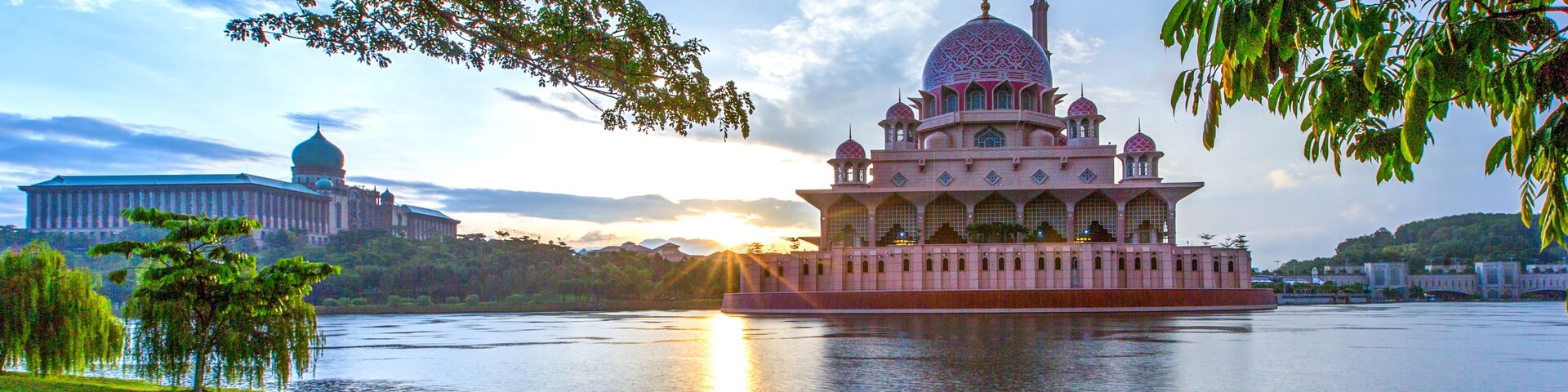 Un edificio grande y ornamentado con una cúpula y varios minaretes, ubicado junto a una masa de agua tranquila.
