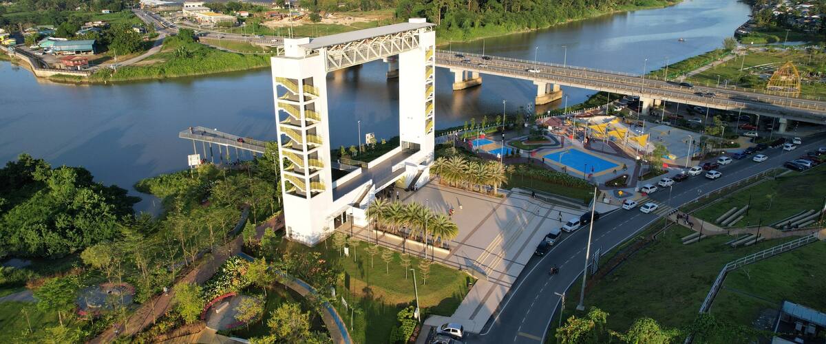 A large white bridge with a unique arch design spanning a river, surrounded by greenery and urban development.