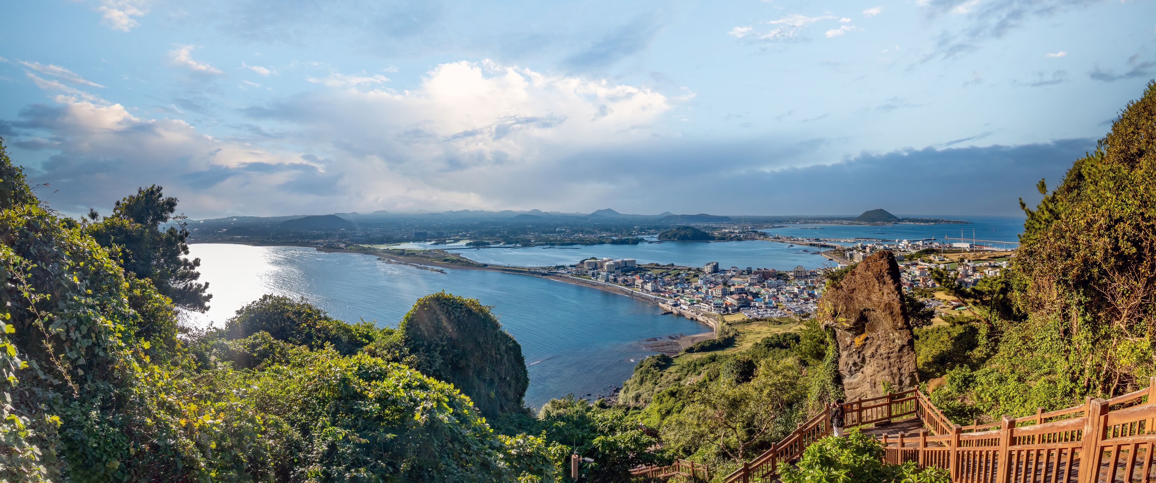 A coastal city with a prominent cliff, a bay, and a distant mountain.
