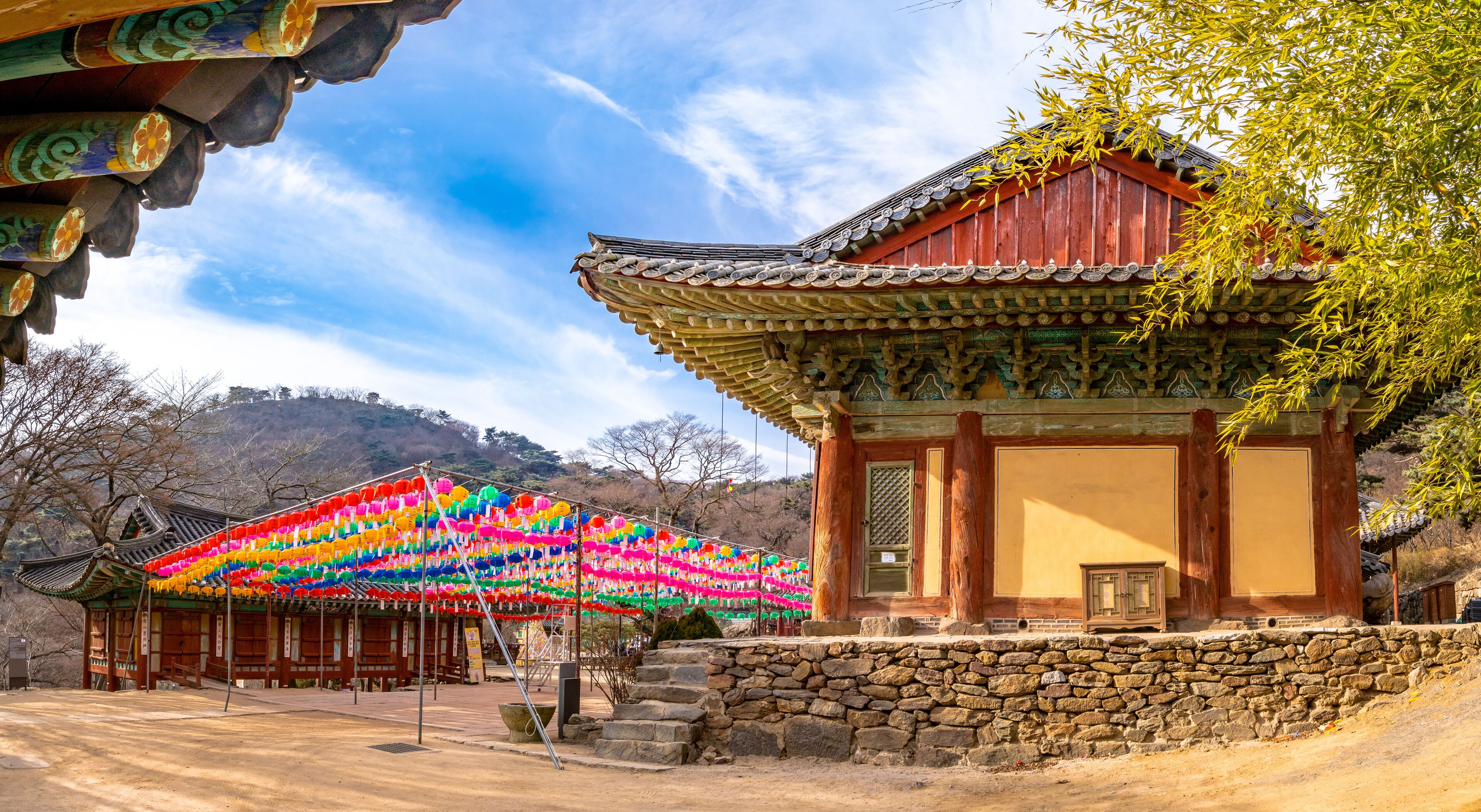 A traditional Korean pavilion with colorful lanterns, a stone wall, and a mountainous backdrop.