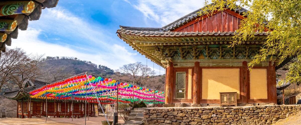 A traditional Korean pavilion with colorful lanterns, a stone wall, and a mountainous backdrop.