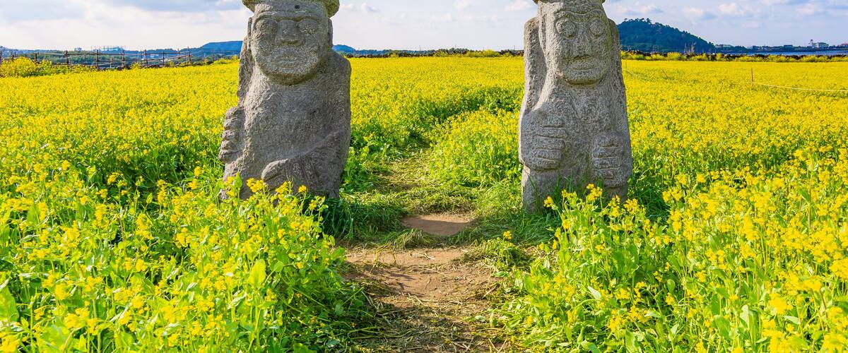 Two large stone statues in a field of yellow flowers under a partly cloudy sky.