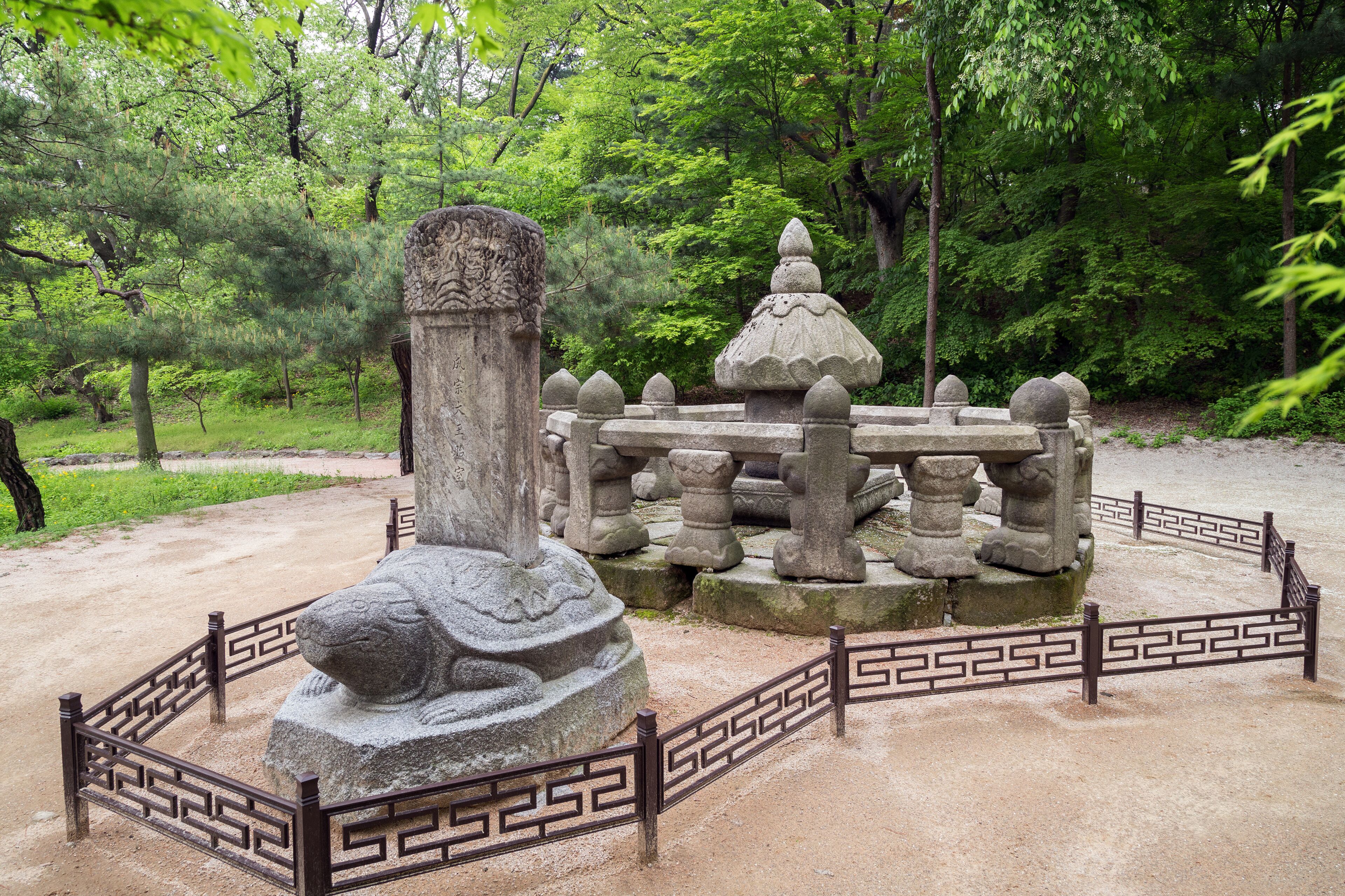 A stone monument with intricate carvings, surrounded by a fence with a geometric pattern.
