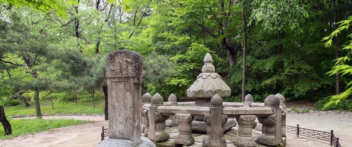 A stone monument with intricate carvings, surrounded by a fence with a geometric pattern.