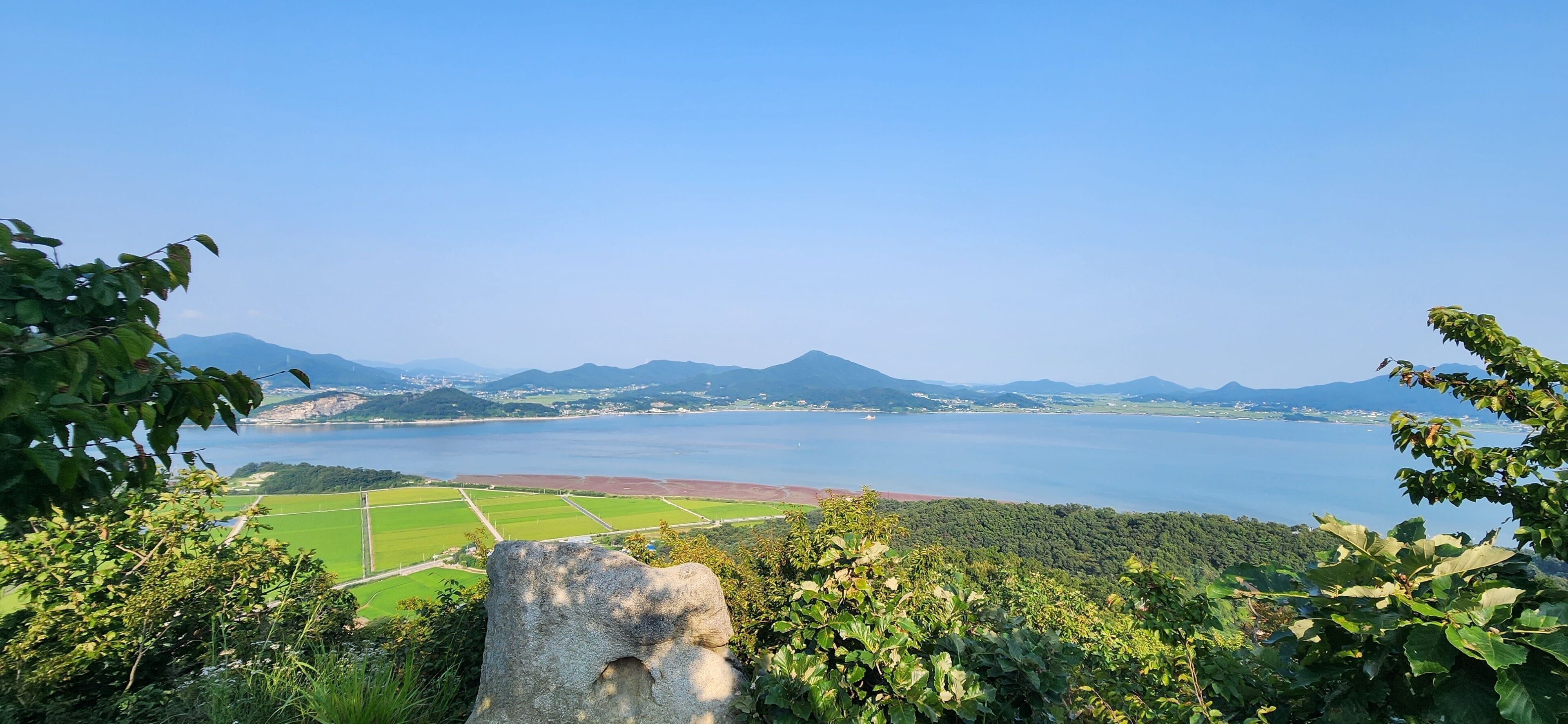 A coastal landscape with a clear view of the sea, green fields, and distant mountains.