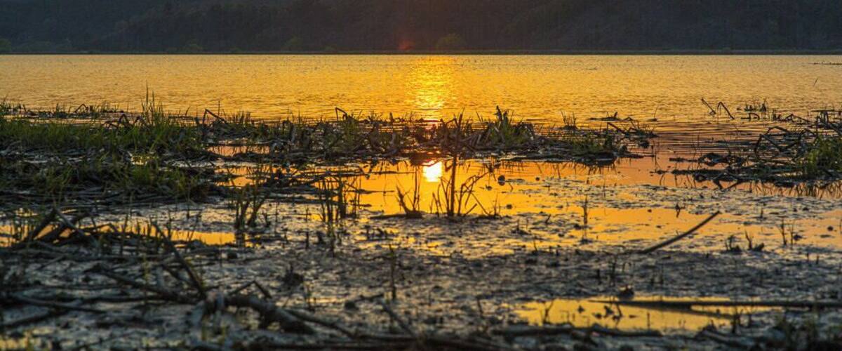 A sunset over a lake with reflections of the sun on the water, surrounded by hills.