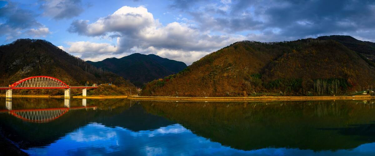 A red bridge over a calm lake with mountains in the background.