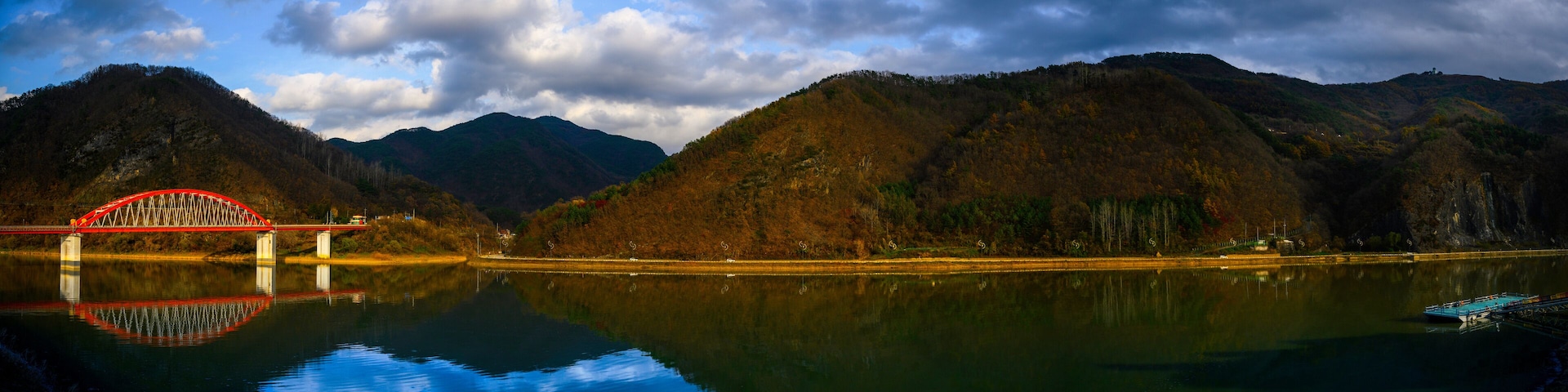 A red bridge over a calm lake with mountains in the background.