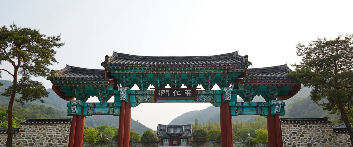 A traditional Korean gate with intricate designs and a stone building in the background.