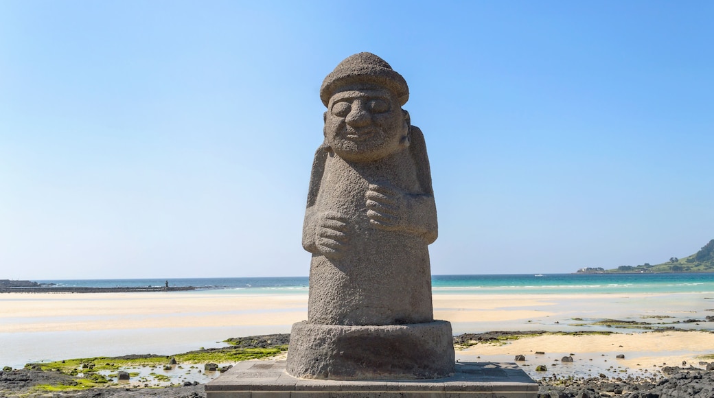 statue of Dol hareubang - symbol of Jeju island on sunny day with sea and beach on background