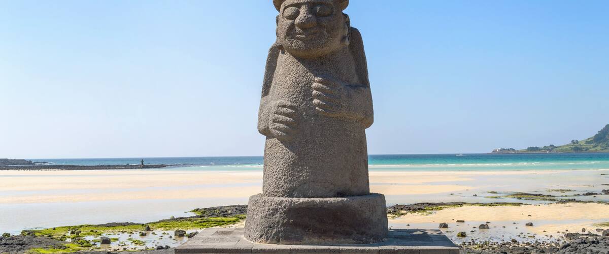 A stone statue on a beach with a clear sky and ocean in the background.