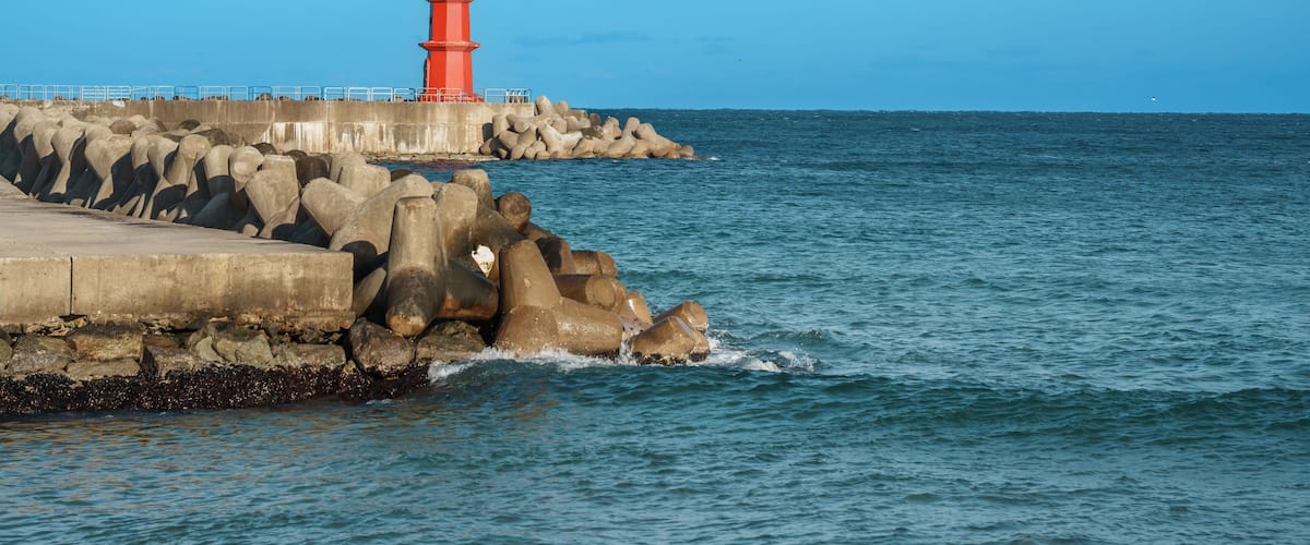 A red lighthouse on a rocky pier with calm sea water.