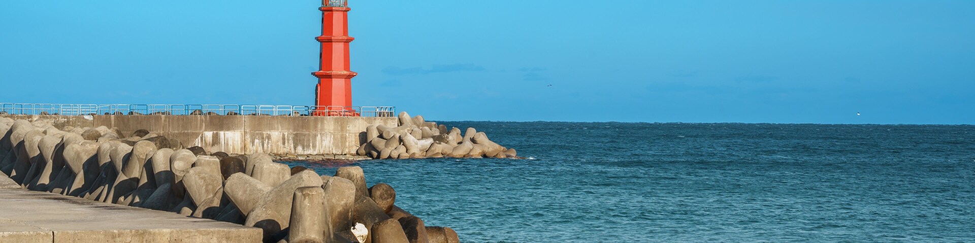 A red lighthouse on a rocky pier with calm sea water.