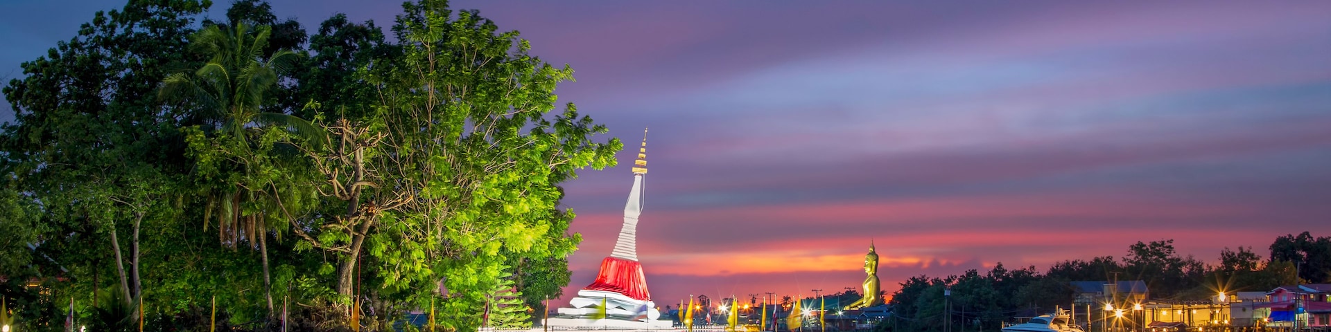 A serene lakeside view at dusk with a prominent pagoda illuminated against a colorful sky, surrounded by lush greenery and calm waters.