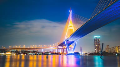 Un puente bien iluminado con una torre, reflejos de luces en el agua.