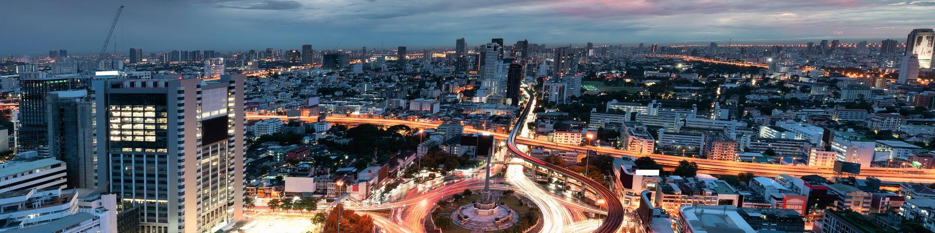 A cityscape at dusk with a prominent roundabout and surrounding high-rise buildings.