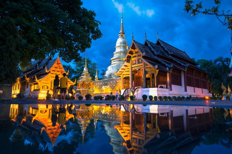 Ein Tempelkomplex mit einer großen Stupa und traditioneller Architektur, der sich in ruhigem Wasser spiegelt.