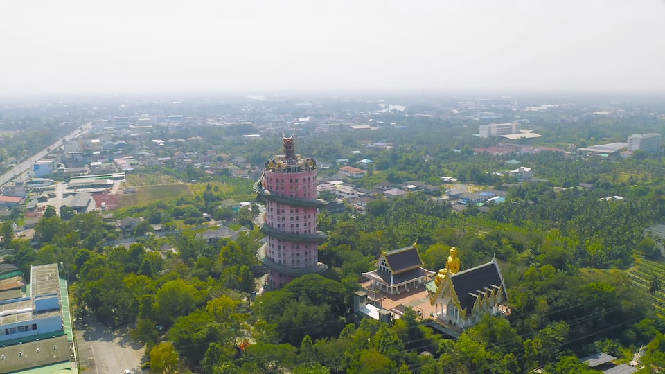 A tower with a golden statue at its base, surrounded by lush greenery and residential buildings.