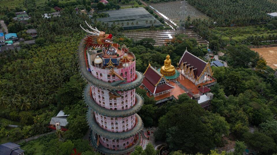 A multi-tiered pagoda with a golden Buddha statue, surrounded by lush greenery and traditional architecture.