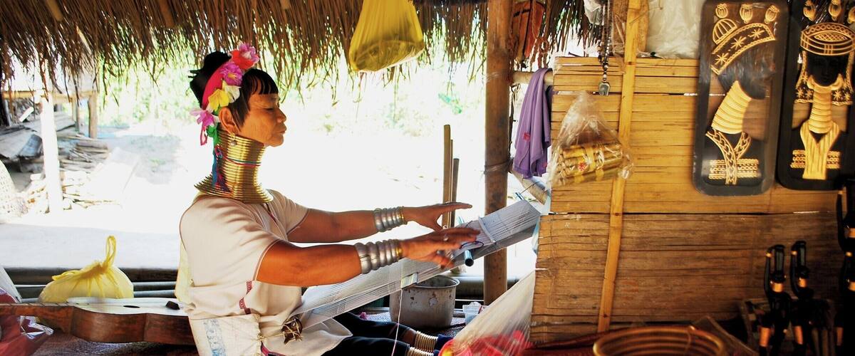 A person weaving at a wooden stall with traditional tools and decorative items.