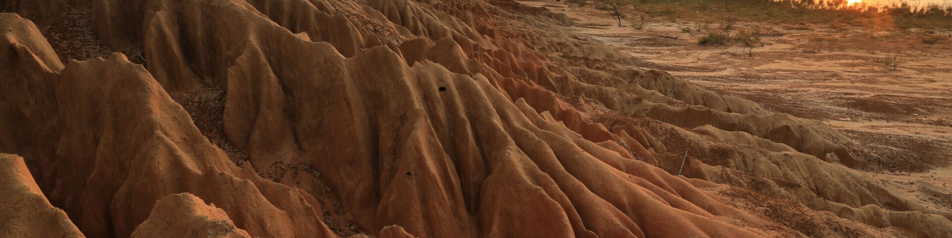Paisagem desértica com formações de areia erodidas e um pôr do sol sobre a água.