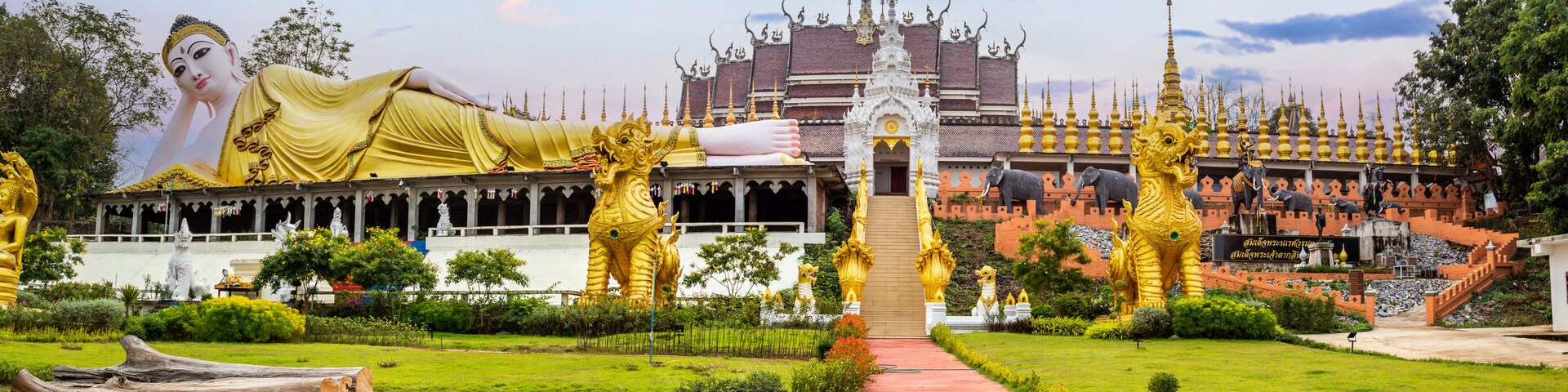 A large golden Buddha statue, a white temple with golden spires, and a pathway leading to the temple.