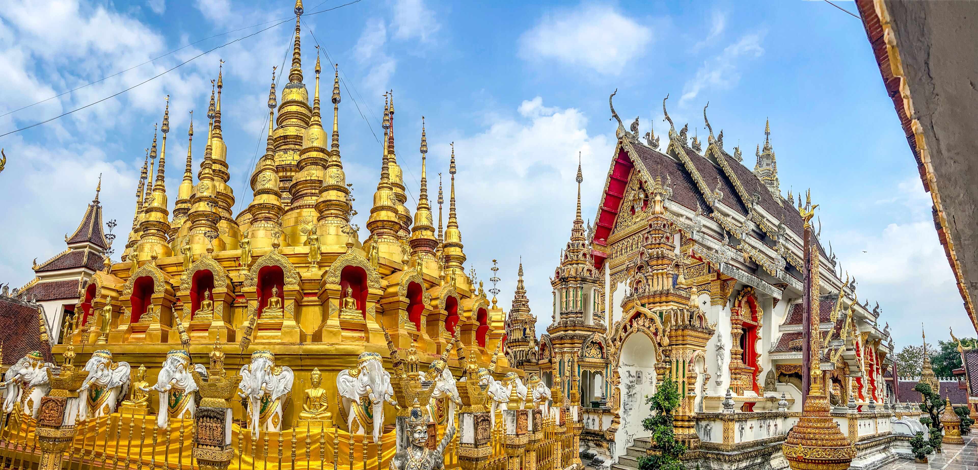 A golden temple with multiple spires and statues, and a white building with red accents.