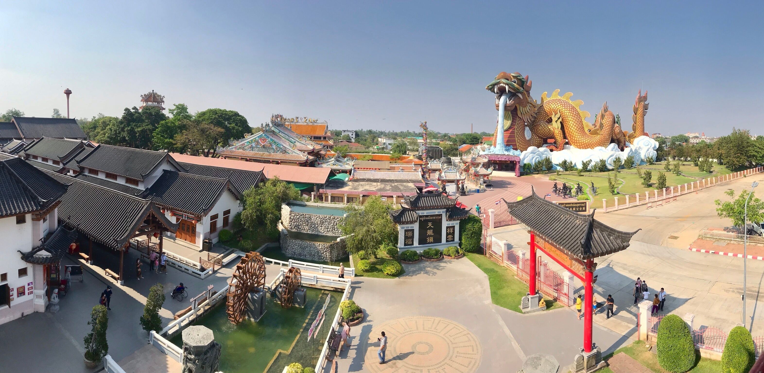 A traditional Chinese architectural complex with pagoda-style buildings, a large dragon sculpture, and a water wheel.