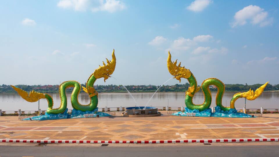 A large dragon sculpture by a river with a tiled plaza in the foreground.
