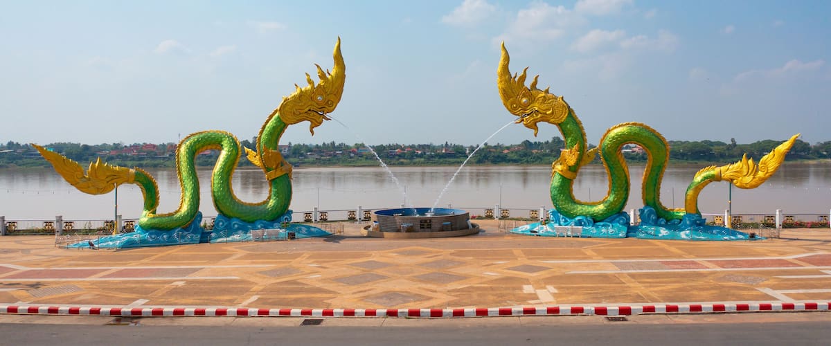 A large dragon sculpture by a river with a tiled plaza in the foreground.