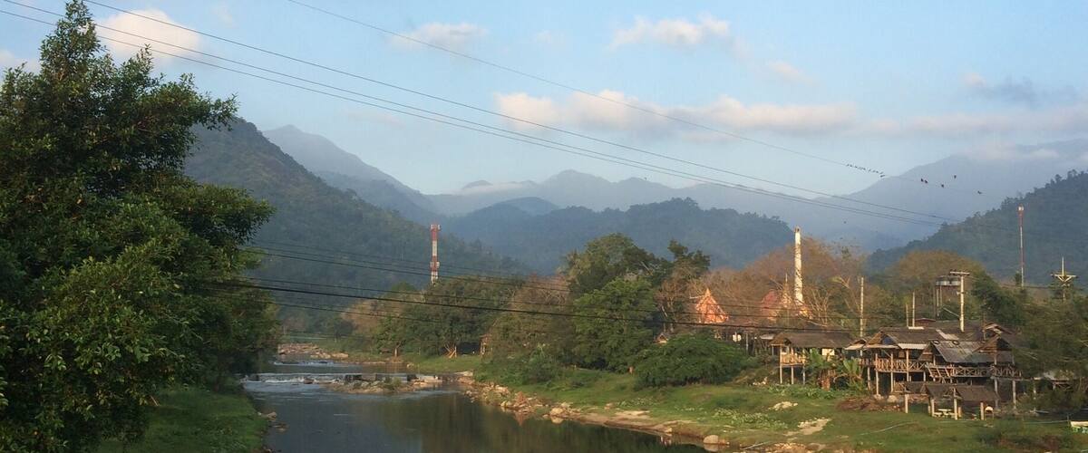 A calm river with a bridge, surrounded by greenery and mountains.