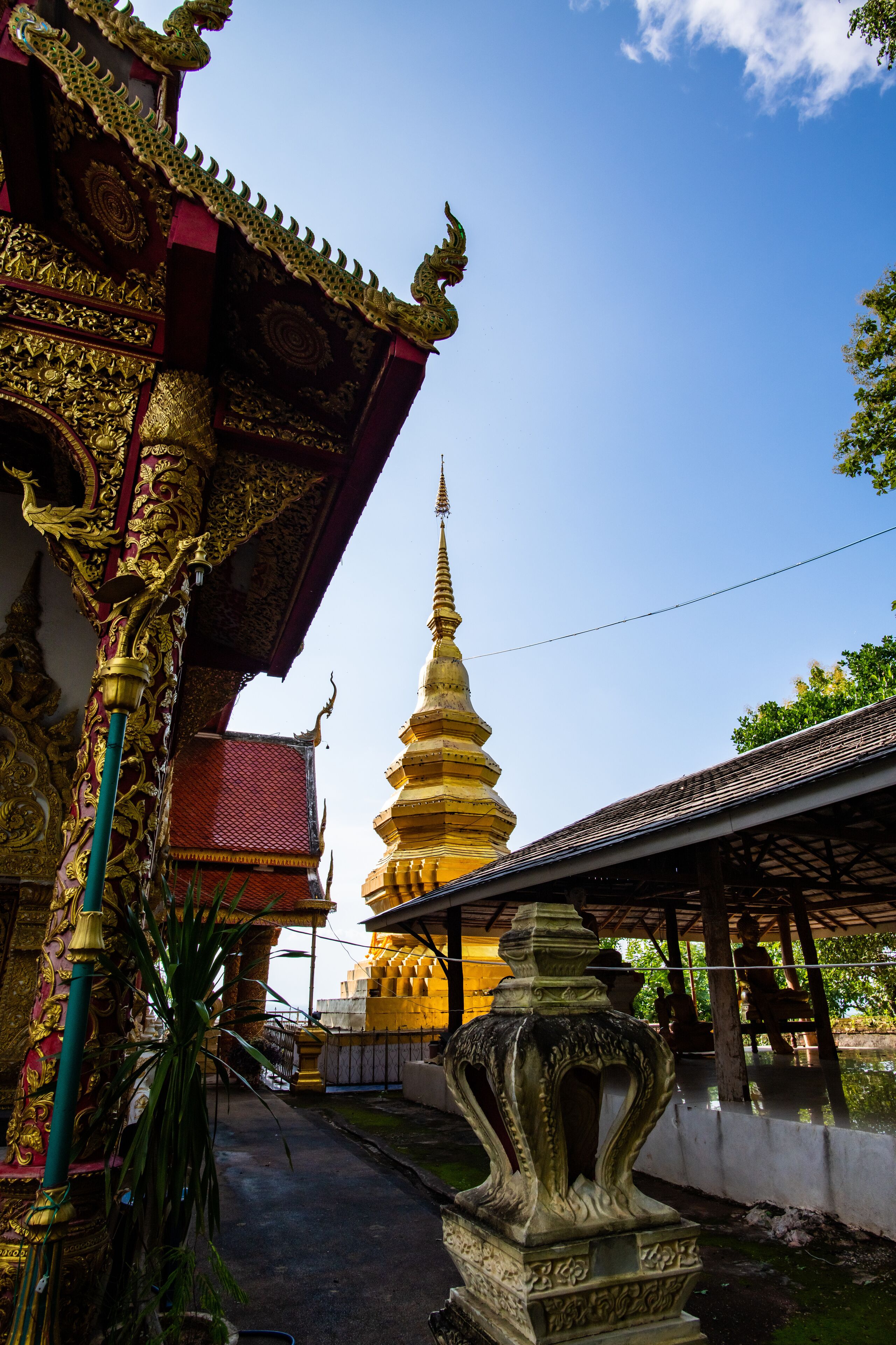 A traditional Thai temple with ornate architecture, a golden stupa, and a covered walkway.
