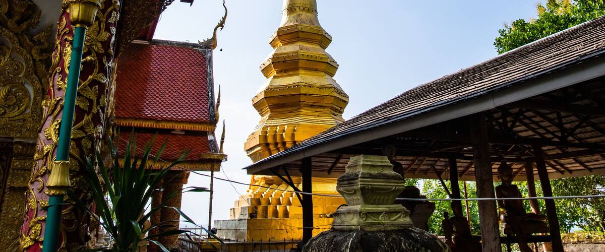A traditional Thai temple with ornate architecture, a golden stupa, and a covered walkway.