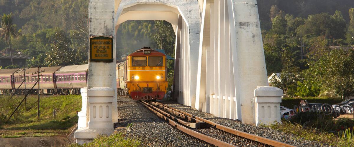 A train passing under a white bridge with a sign that reads "Cambridge 2002."