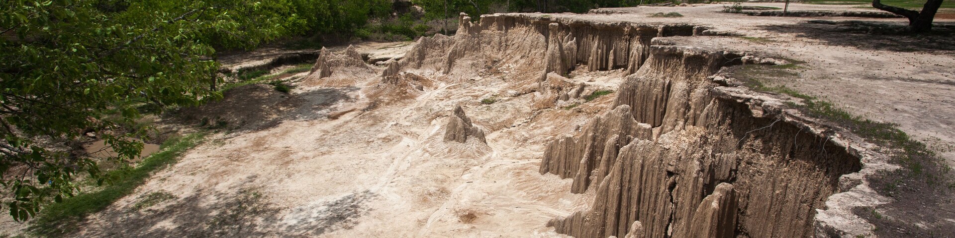 A natural landscape with a large sinkhole surrounded by trees and a cloudy sky.