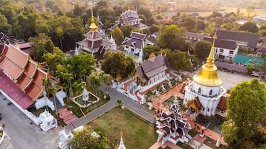 Vista aérea de un complejo de templos con múltiples pagodas, agujas doradas y edificios blancos, todo rodeado de exuberante vegetación.