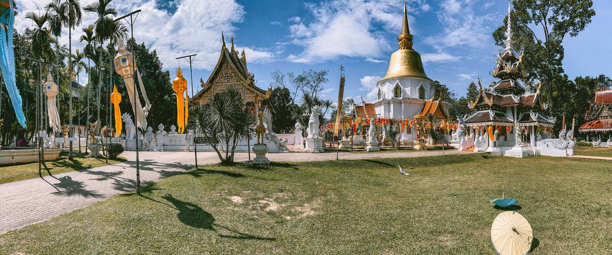 A temple complex with a large golden dome, traditional Thai architecture, and surrounding greenery.