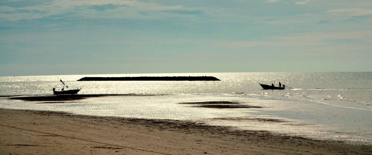 A beach with two boats and a breakwater.