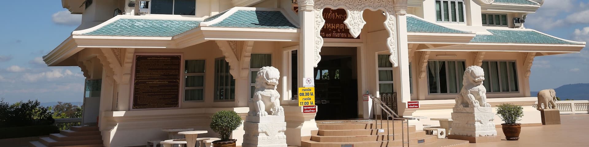 A traditional Thai temple with ornate architecture, including a multi-tiered roof and lion statues at the entrance.