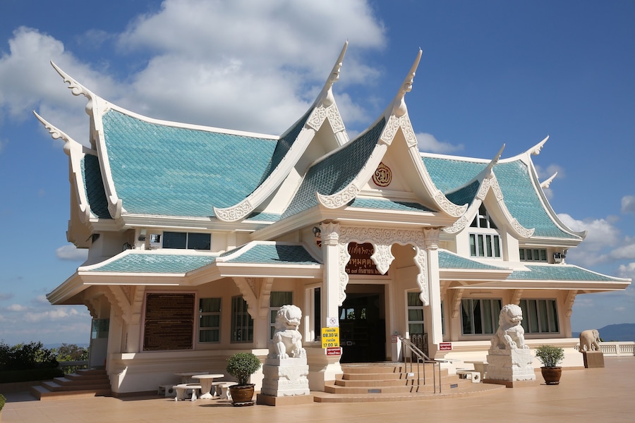 A traditional Thai temple with ornate architecture, including a multi-tiered roof and lion statues at the entrance.